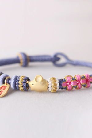Golden rat charm on handwoven zodiac bracelets with periwinkle and pink threads.